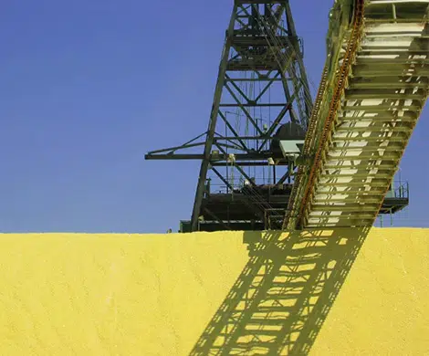 Grande mucchio di materiale giallo, trasportatore e struttura metallica.